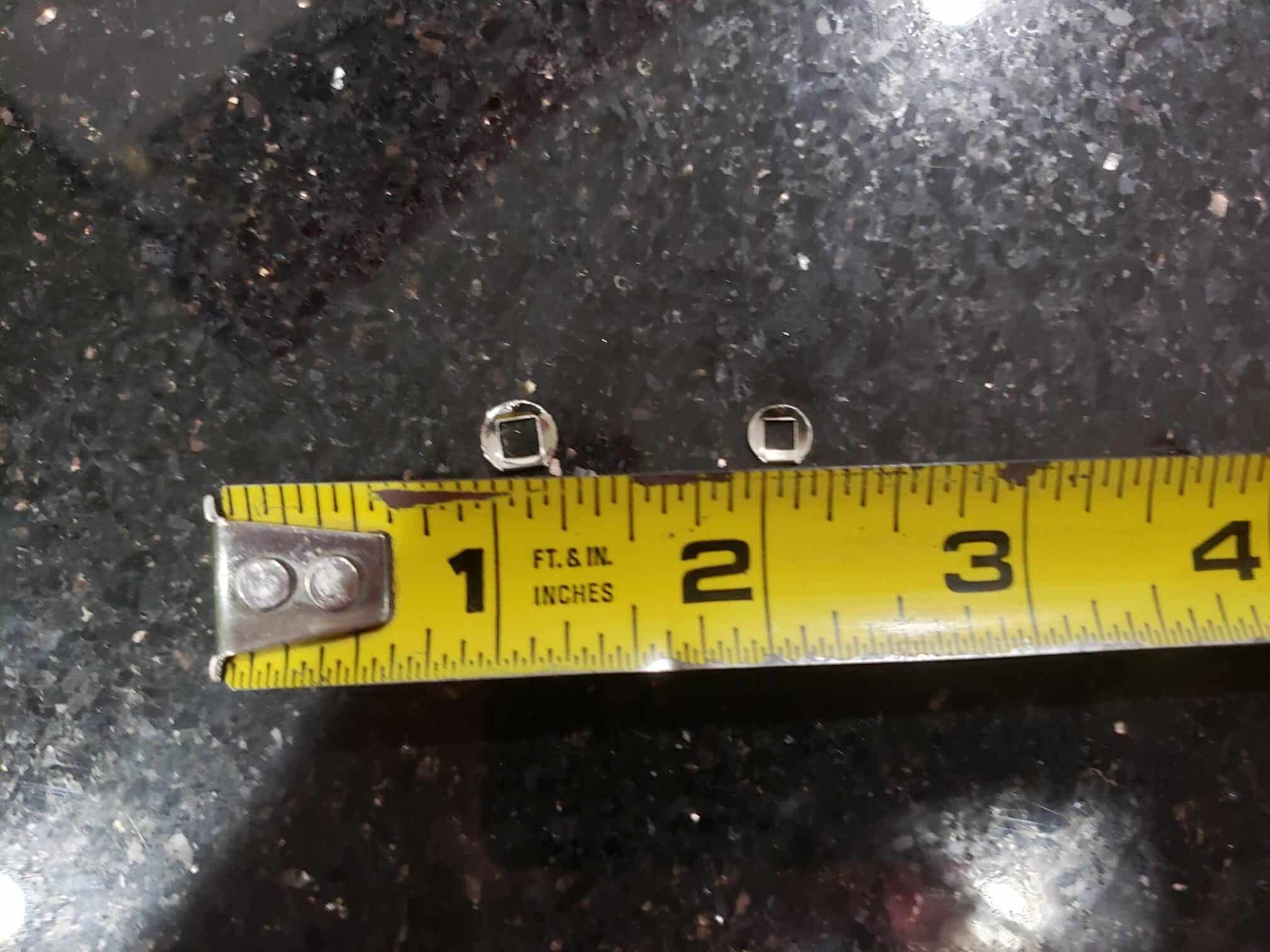 A tape measure beside two Internal Click Plates on a black speckled surface shows the plates are about 1.5 inches long.
