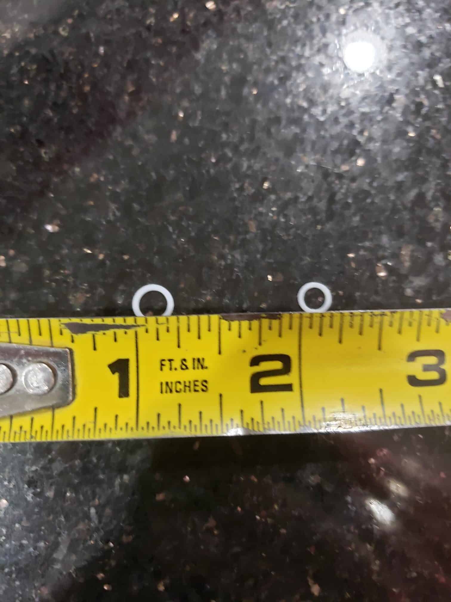 Two small white Washers rest on a black countertop with a yellow tape measure showing their diameter is just under 1/4 inch.